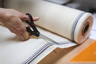 Ausgeschnittenes Bild von handgeschnittenem Stoff mit einer Schere auf einem Tisch in einer Werkstatt - CAVF47274