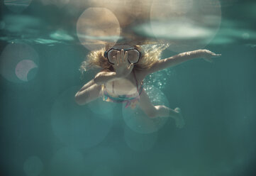 Carefree girl wearing goggles while swimming underwater in pool - CAVF47316