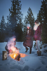 Female friends making camp fire on snow covered field - CAVF47324