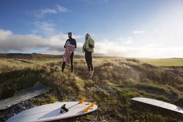 Surfer schauen weg, während sie auf einer Wiese vor dem Himmel stehen - CAVF47343