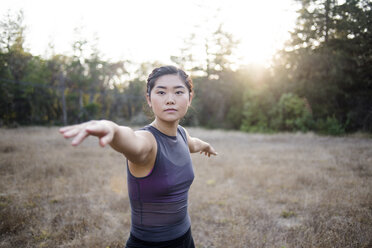 Portrait of confident woman with arms outstretched practicing yoga at field - CAVF47380