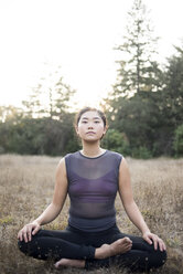 Porträt einer selbstbewussten Frau, die im Schneidersitz auf einem Feld Yoga übt - CAVF47381