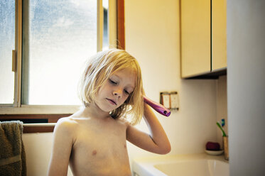 Thoughtful shirtless boy combing hair in bathroom - CAVF47386