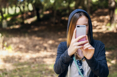 Teenagerin fotografiert im Park mit ihrem Smartphone - CAVF47390