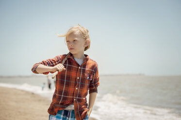 Nachdenklicher Junge, der einen Stock hält, während er am Strand spazieren geht - CAVF47391