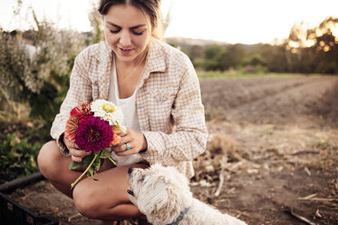 Female farmer holding beautiful flowers with dog on field - CAVF47428
