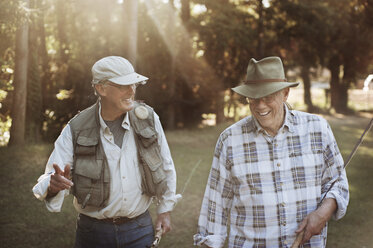 Glückliche ältere Männer halten Angelruten beim Spaziergang im Wald - CAVF47455