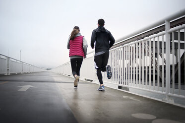 Rückansicht von Sportlern, die auf der Bay Bridge gegen den Himmel laufen - CAVF47460