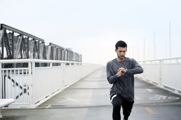 Selbstbewusster männlicher Sportler, der beim Training auf der Bay Bridge gegen den klaren Himmel die Zeit überprüft - CAVF47464