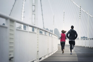 Rückansicht von Sportlern, die auf der Bay Bridge gegen den Himmel laufen - CAVF47468