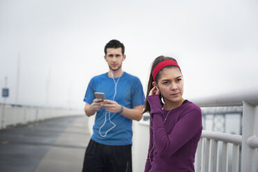 Selbstbewusste Sportlerin mit Kopfhörern, während sie mit einem Freund auf der Bay Bridge steht - CAVF47469