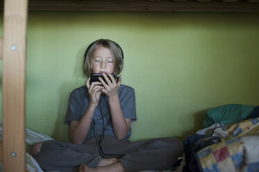 Front view of boy using smart phone while sitting on bed - CAVF47475