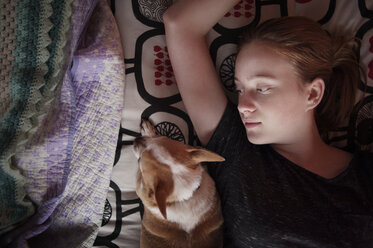 Overhead view of girl lying by dog on bed at home - CAVF47486