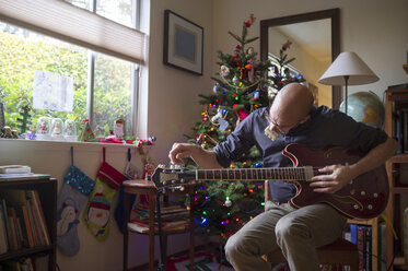 Mann mit Gitarre zu Hause in der Weihnachtszeit - CAVF47491