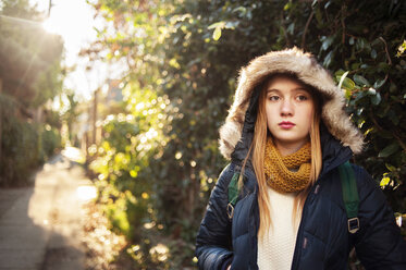 Girl wearing warm clothing and standing against trees - CAVF47500