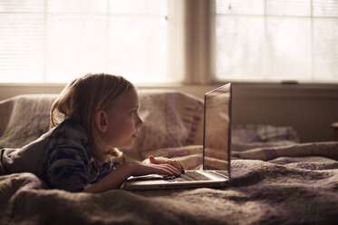 Junge benutzt Laptop, während er zu Hause auf dem Bett liegt - CAVF47503