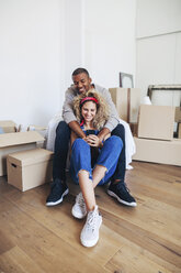 Happy couple using mobile phone while sitting at new home - CAVF47551