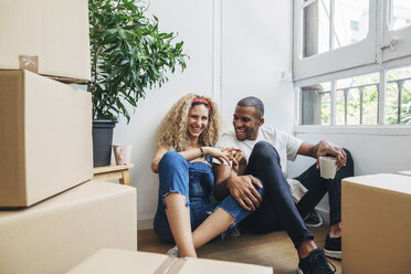 Happy couple talking while having drinks by wall in new house - CAVF47577