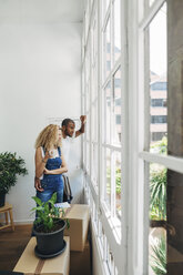 Couple looking through window while standing in new house - CAVF47579