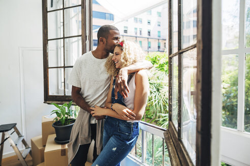 Ehemann küsst Frau auf die Stirn, während er am Fenster eines neuen Hauses steht - CAVF47582