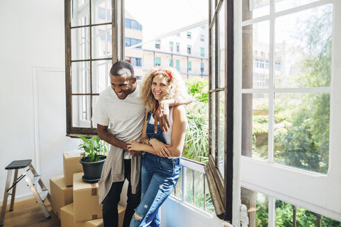 Portrait of cheerful wife standing with husband by window in new house - CAVF47583