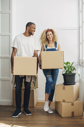 Glückliches Paar, das Kartons trägt, während es auf dem Boden seines neuen Hauses steht - CAVF47589