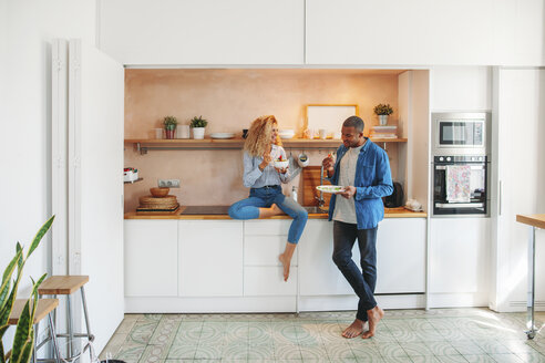 Volles Bild eines glücklichen multiethnischen Paares, das in der Küche Salat und Sandwich isst - CAVF47594