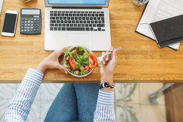 Draufsicht auf eine Frau, die eine Salatschüssel neben einem Laptop an einem Holztisch hält - CAVF47600