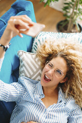 Hohe Winkel Ansicht der fröhlichen jungen Frau, die Selfie durch Smartphone, während auf dem Sofa zu Hause liegen - CAVF47608