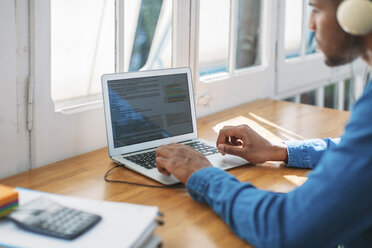 Cropped image of young man blogging through laptop computer at table by window - CAVF47619