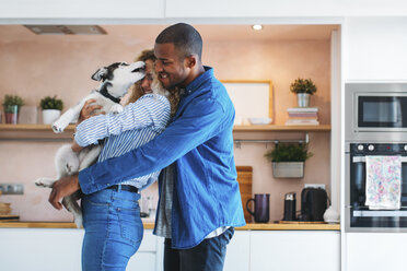 Affectionate multi-ethnic couple playing with Siberian Husky at home - CAVF47622