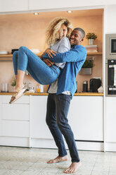 Full length of cheerful man carrying woman in kitchen at home - CAVF47623
