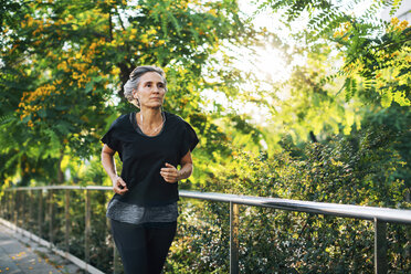 Woman looking away while jogging on footpath - CAVF47626