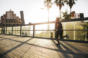 Rear view of woman jogging on bridge during sunset - CAVF47627