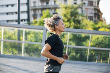 Side view of woman jogging while listening music at bridge - CAVF47630