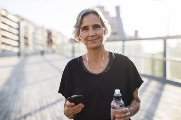Porträt einer selbstbewussten Frau mit Smartphone und Wasserflasche auf einer Brücke - CAVF47633