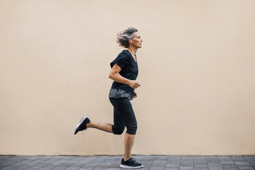 Side view of woman jogging on footpath against wall - CAVF47635