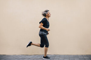 Seitenansicht einer Frau, die auf dem Gehweg gegen eine Wand joggt - CAVF47635