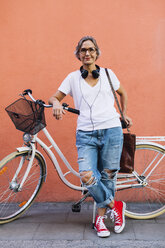 Porträt einer selbstbewussten Frau mit Fahrrad, die an der Wand steht - CAVF47645