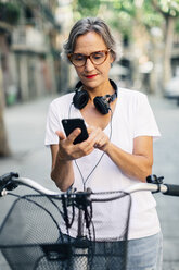 Frau benutzt Smartphone, während sie mit dem Fahrrad auf der Straße steht - CAVF47649