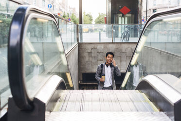 Geschäftsmann, der mit seinem Smartphone telefoniert, während er auf einer Rolltreppe steht - CAVF47661