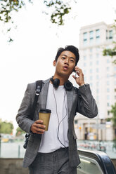 Businessman talking on smart phone while holding disposable cup in city - CAVF47662