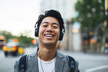 Portrait of happy businessman listening music in city - CAVF47671