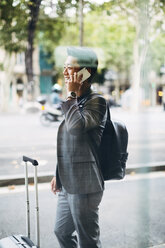 Geschäftsmann mit Gepäck, der durch ein Fenster gesehen mit seinem Smartphone telefoniert - CAVF47672