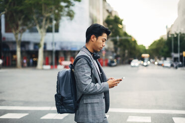 Seitenansicht eines Geschäftsmannes mit Rucksack, der ein Smartphone benutzt, während er auf der Straße steht - CAVF47673