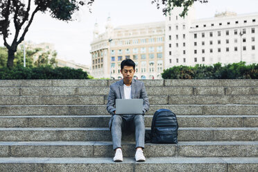 Geschäftsmann, der einen Laptop benutzt, während er mit einer Tasche auf den Stufen sitzt - CAVF47674