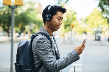 Geschäftsmann mit Rucksack, der sein Smartphone benutzt, während er auf dem Fußweg Musik hört - CAVF47683