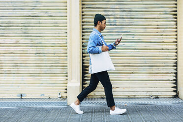 Man using smart phone while walking against shutter - CAVF47690