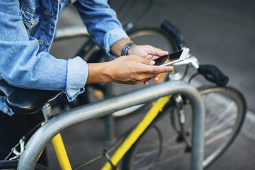 Abgeschnittene Hände eines Mannes, der sein Smartphone am Fahrrad benutzt - CAVF47695