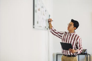 Businessman holding clipboard while writing on whiteboard in office - CAVF47717